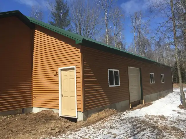 Long brown-sided building with a green metal roof and a service door