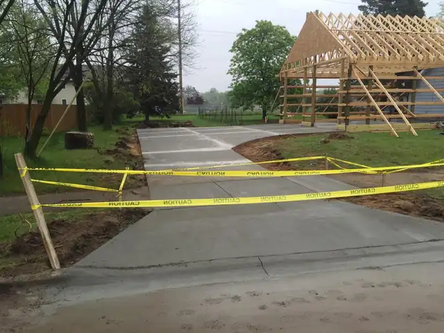 Finished concrete driveway pour behind caution tape with a pole-frame building in the background