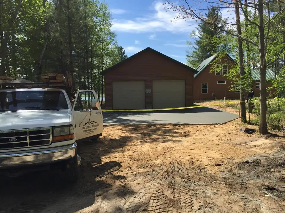 The crew's white Ford with JDC Construction lettering on the door, parked by a new two-car garage and its fresh concrete apron