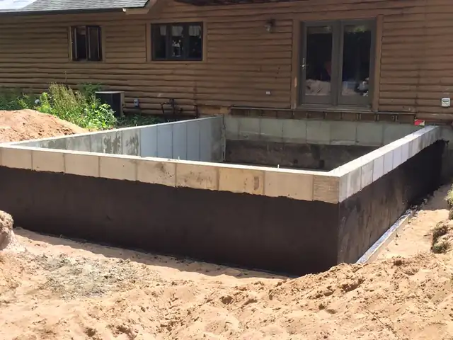 Waterproofed block foundation with forms set beside a home