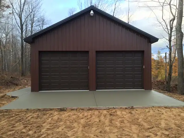 Maroon two-door garage on a new concrete apron, autumn trees behind