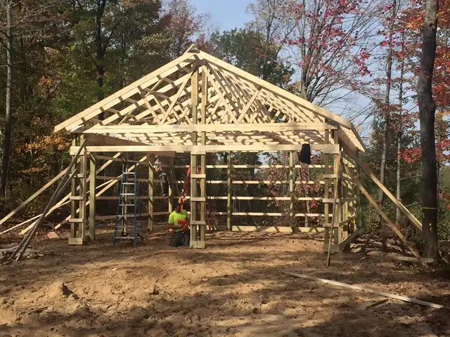 Pole barn truss framing going up, one worker small in the frame