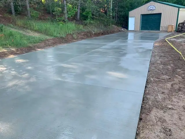 A long smooth concrete drive running to a green-doored pole building